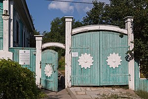 На фото изображены украшенные объёмными декоративными элементами бело-зелёные ворота, ведущие на приусадебный участок дома, в котором жил и работал художник А. Э. Тюлькин